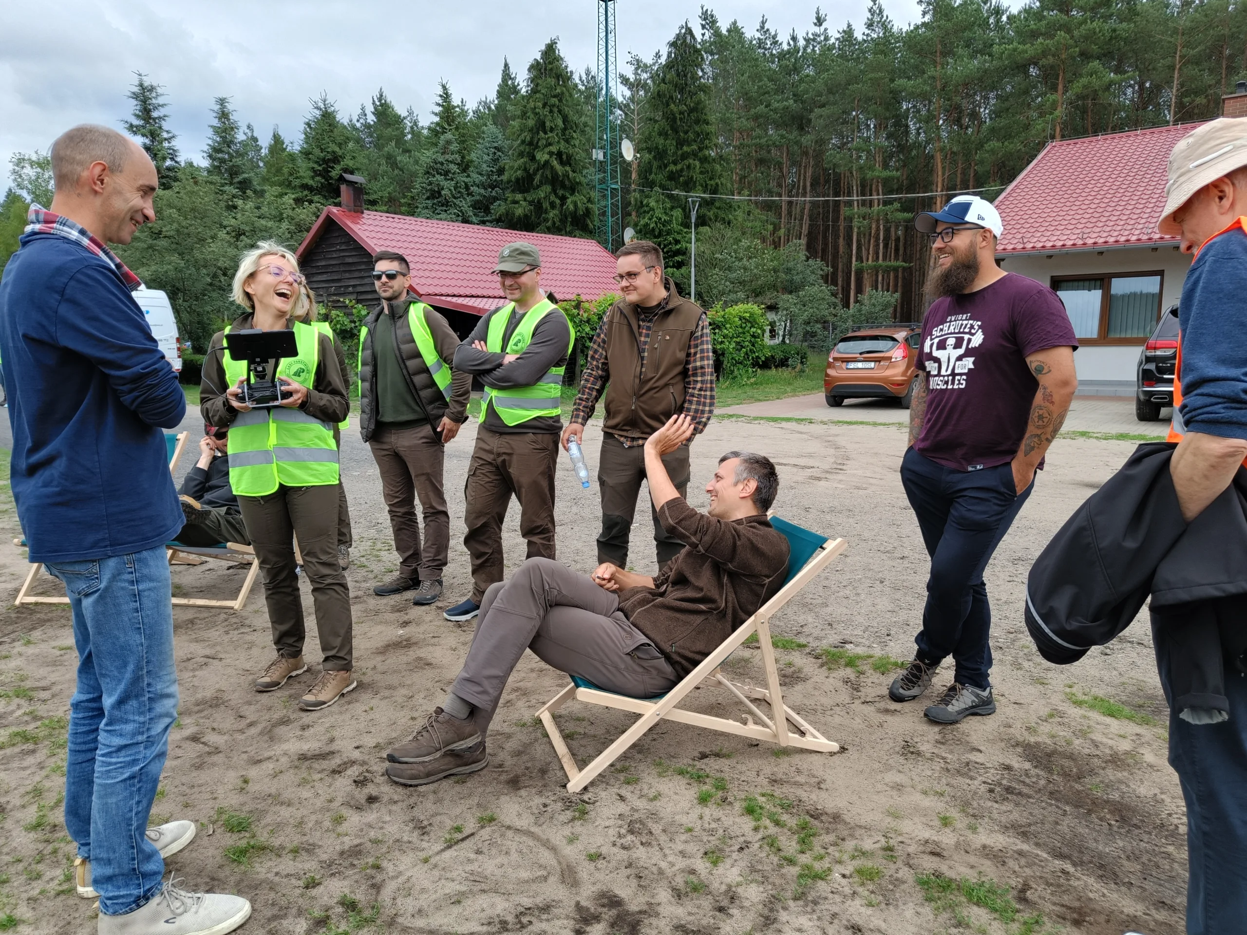 Roześmiana grupa kursantów i instruktorów Era Dronów podczas przerwy między lotami na szkoleniu dronowym — w tle leżaki i baza szkoleniowa